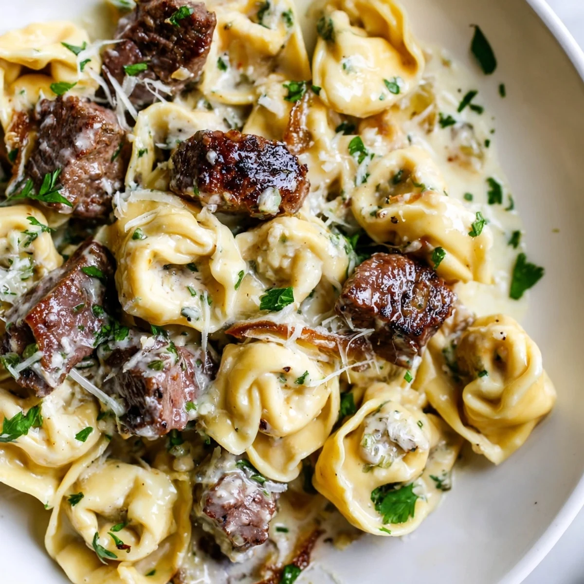 Steaming bowl of garlic steak tortellini glistening with a velvety cream sauce and herbs