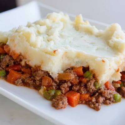 A spoon lifting a serving of Beef Shepherds Pie with Creamy Cauliflower Mash reveals a rich, savory beef and pea filling.