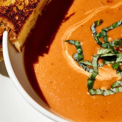 Hearty Creamy Tomato Basil Bisque with Grilled Cheese Soldiers alongside, with buttery bread, melted cheddar, and fresh basil.