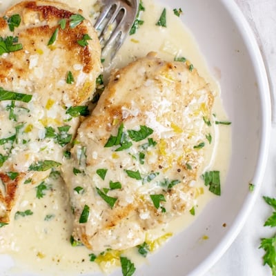 Tender golden chicken breasts bathed in a rich Creamy Parmesan Lemon Chicken sauce, garnished with parsley and lemon zest.