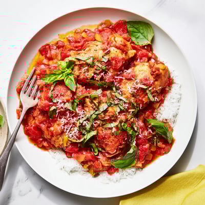 Tender chunks of Slow Cooker Tomato Basil Chicken are served over a bed of creamy polenta, with fresh basil and a side of crusty Italian bread nearby.