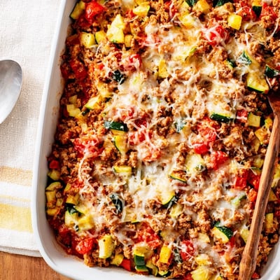 A close-up of bubbly Easy Ground Turkey Zucchini Casserole showing layers of ground turkey, diced zucchini, and red bell pepper.