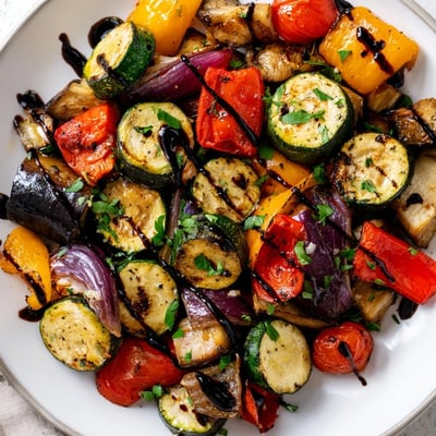 A close-up of golden brown Italian Roasted Vegetables, highlighting caramelized tomatoes and onions on a rustic wooden table.