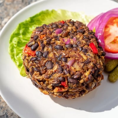 A close-up of a homemade Mushroom Veggie Burger patty with lettuce, tomato, and pickles on a brioche bun.