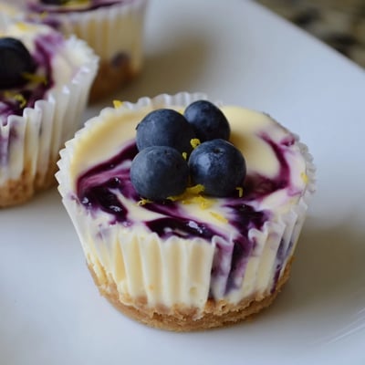 Golden graham crust cradles smooth mini lemon blueberry cheesecakes swirled with purple blueberry sauce